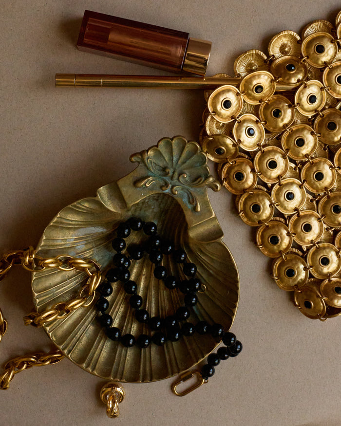 Gold necklace with black beads and decorative elements on a beige background