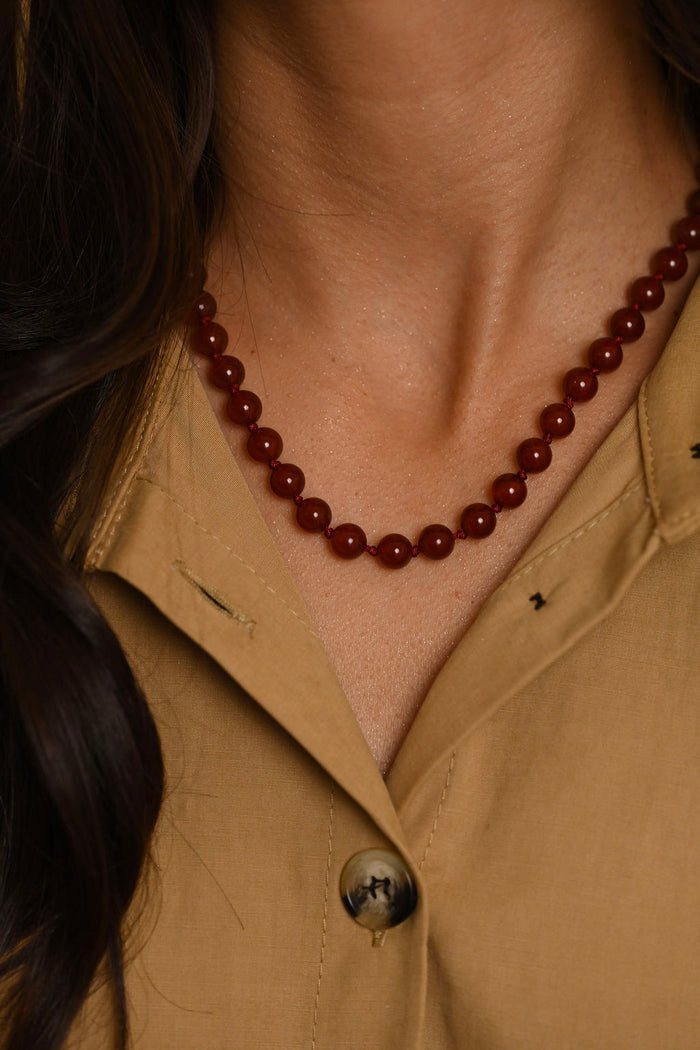 Close-up of a person wearing a brown beaded necklace and beige shirt.