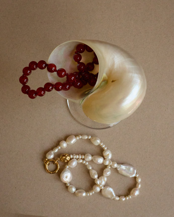 Red beaded necklace and white pearl necklace on a beige surface