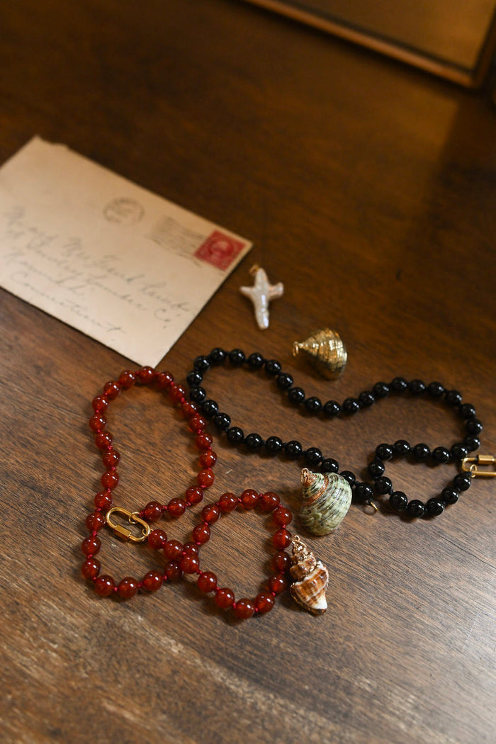 Two beaded necklaces on a wooden surface with an envelope and small gold object.