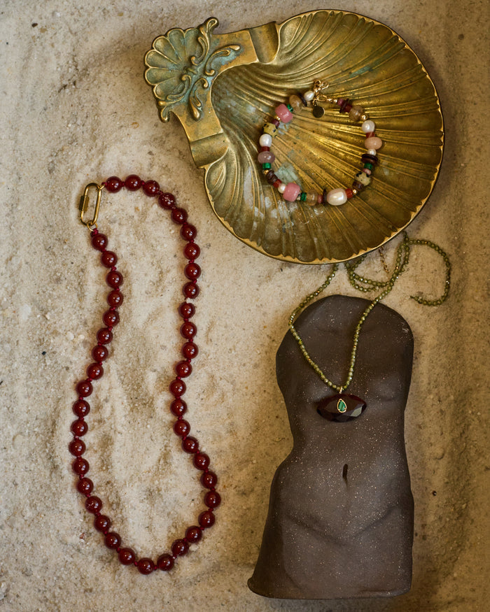 Jewelry display with a gold shell, beads, and a mannequin torso on a textured surface.