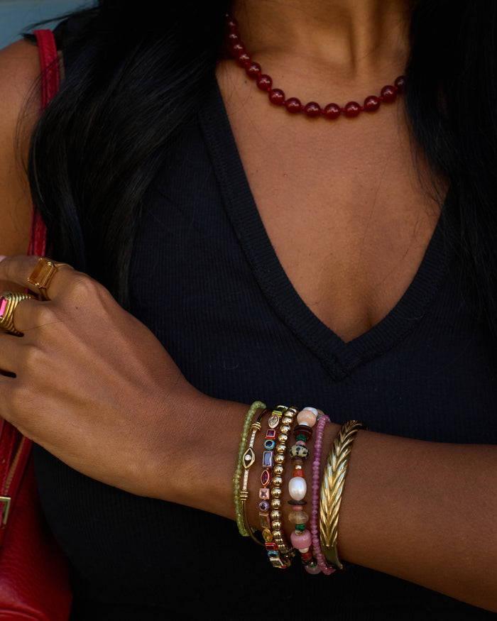 Close-up of a person's arm wearing multiple colorful bracelets and a ring, with a dark background.