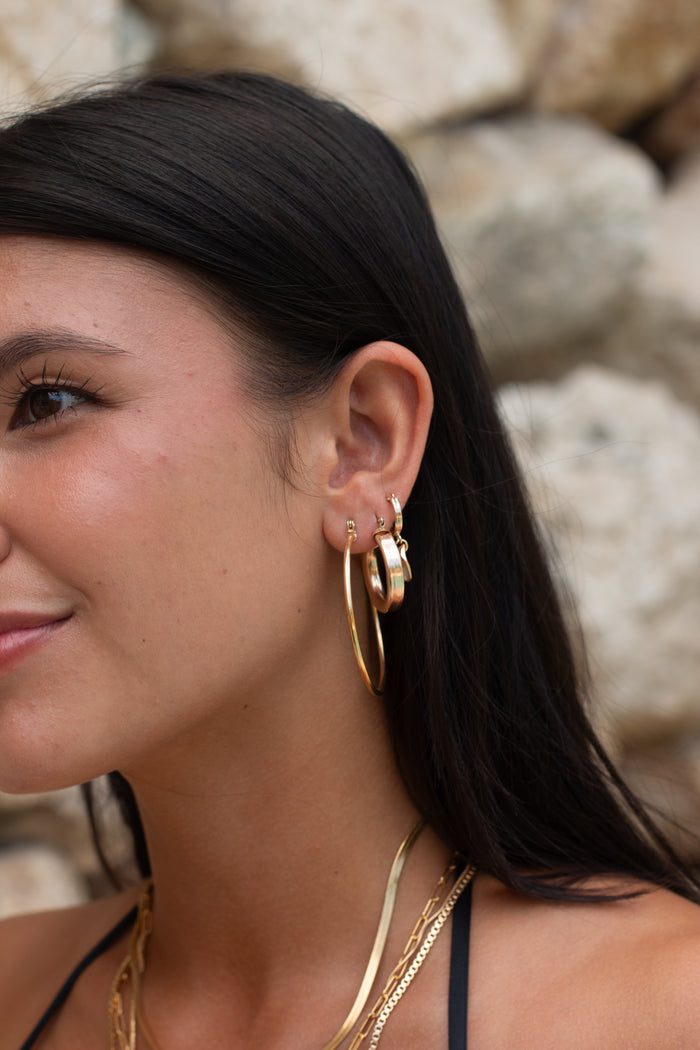 A woman wearing simple gold hoop earrings and layering necklaces