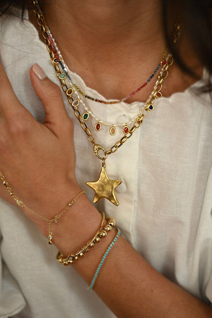 Close-up of a person wearing multiple gold necklaces and bracelets on a white background