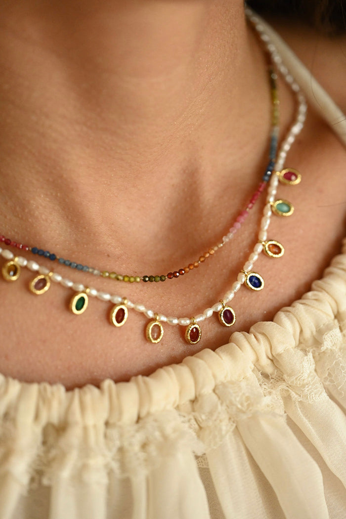 Necklace with colorful beads and pearls worn by a person in a cream-colored garment.