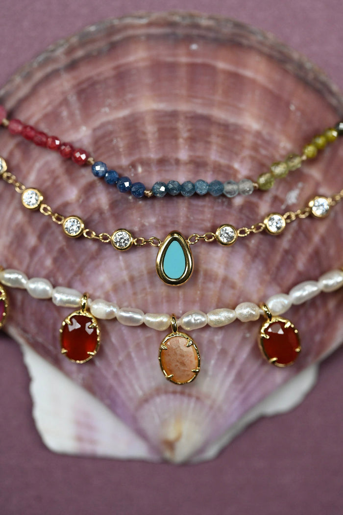 Stack of colorful beaded and gemstone necklaces on a seashell background