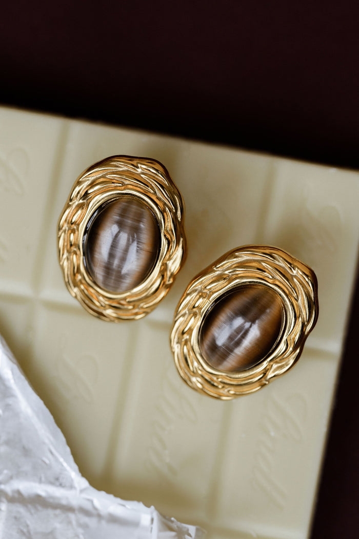 Gold earrings with brown stones on a textured surface