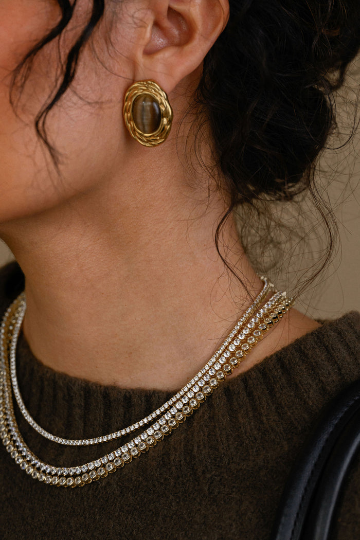 Close-up of a person wearing gold earrings and layered necklaces.