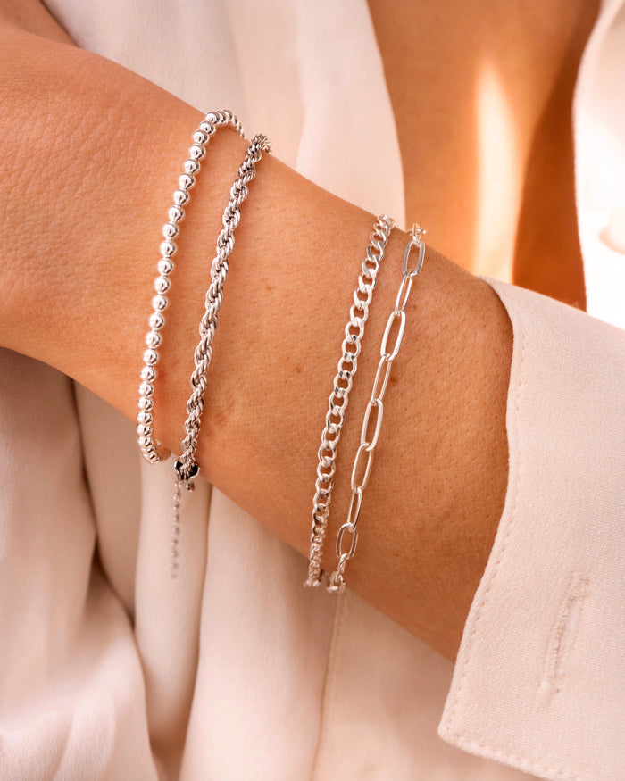 Close up of a person in a white shirt wearing dainty silver bracelets on their wrist
