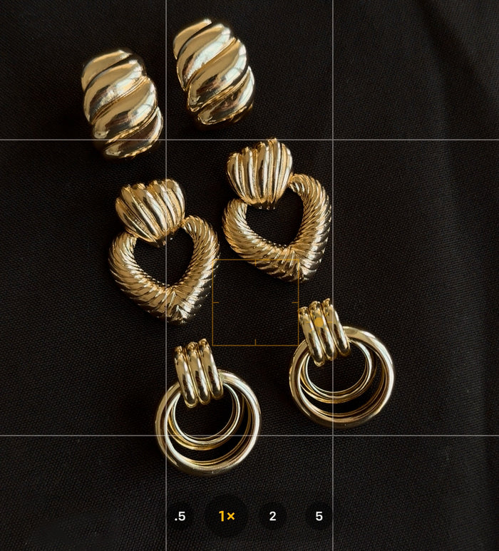 Close up of three pairs of gold earrings on a black fabric background
