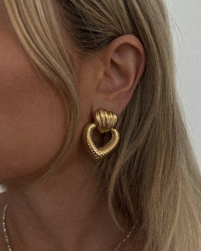 A woman wearing gold heart earrings