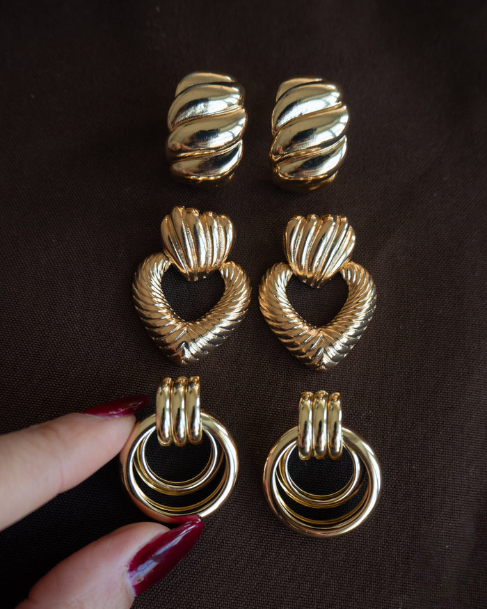 Close up of three pairs of gold earrings on a black fabric background