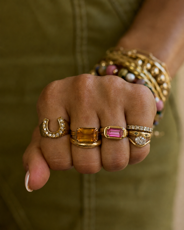 Hand wearing multiple gold rings with gemstones against a green background