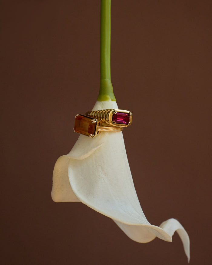 Gold ring with a red gemstone on a white flower against a brown background