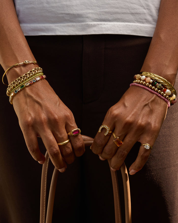 Close-up of hands wearing multiple bracelets and rings with a dark background