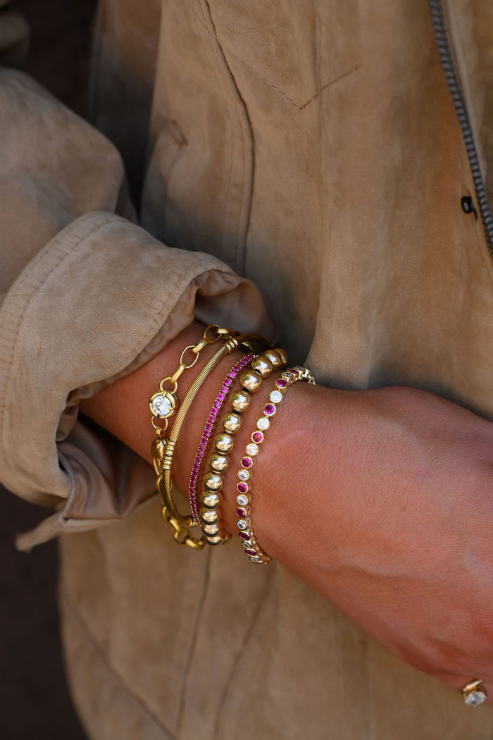 A person wearing a suede jacket and assorted gold and stone bracelets