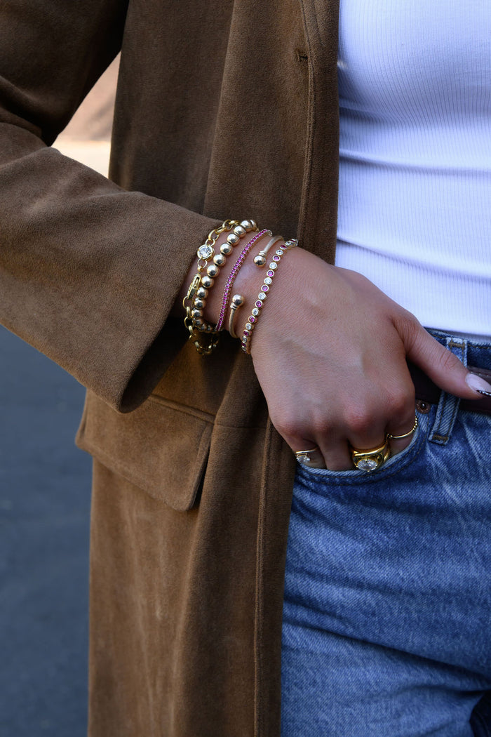 A hand with gold rings and bracelets tucked into a pair of jeans