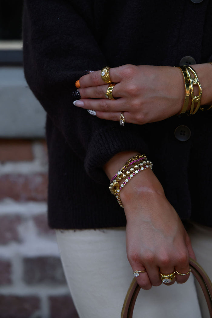 A person wearing gold rings and bracelets holding a purse