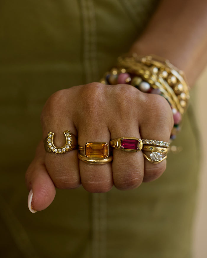 Close-up of a hand wearing multiple gold rings with gemstones against a blurred background.