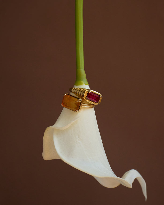 Gold ring with a red gemstone on a white flower against a brown background