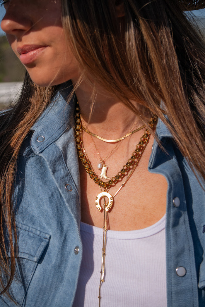 Close-up of a person wearing multiple gold necklaces with a denim jacket and white top.