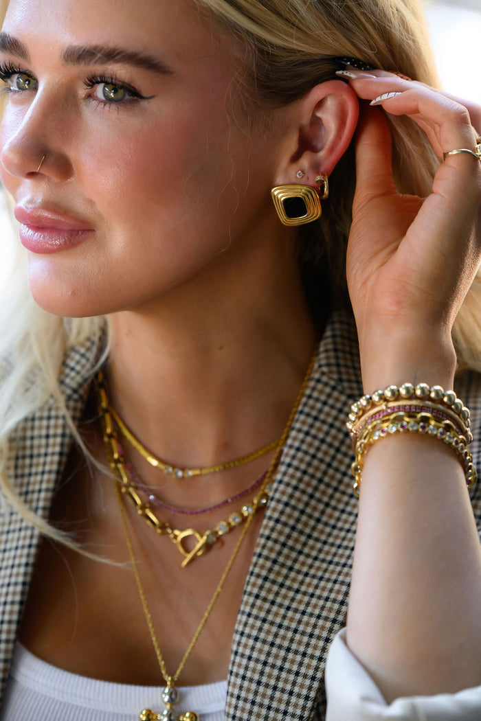 A woman in a blazer wearing statement gold earrings, bracelets, and necklaces