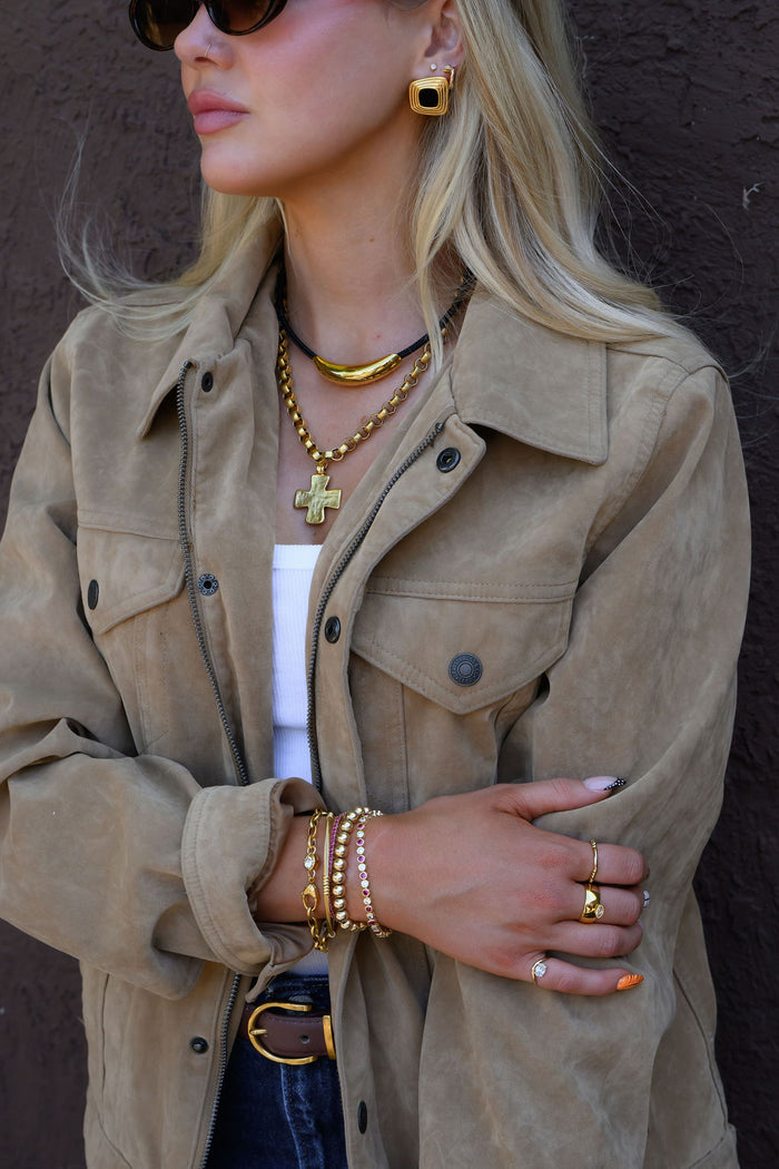 A woman wearing a bold pair of earrings and necklaces in a tan jacket and jeans