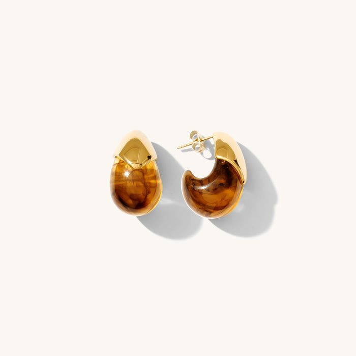 Close up shot of gold and resin earrings on a white background