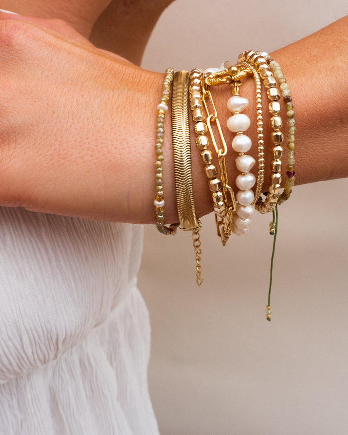 A person's wrist with gold and pearl bracelets resting on their white top