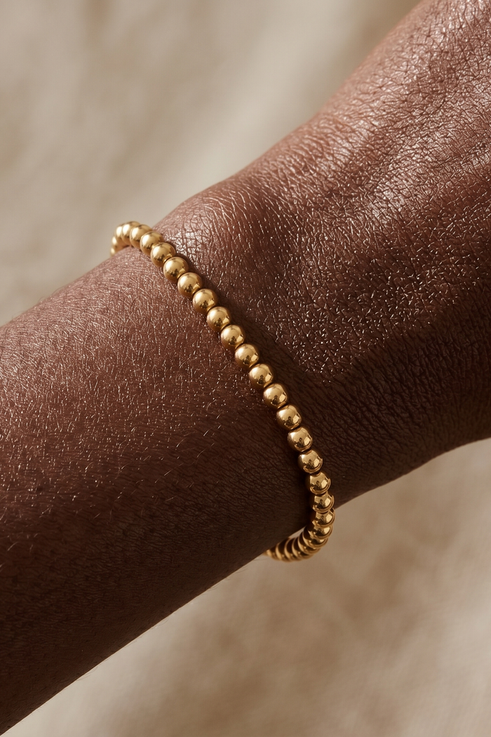 Gold beaded bracelet on a wrist with a neutral background