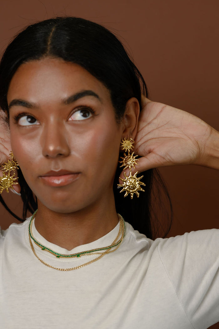 Woman wearing statement gold earrings on a brown background