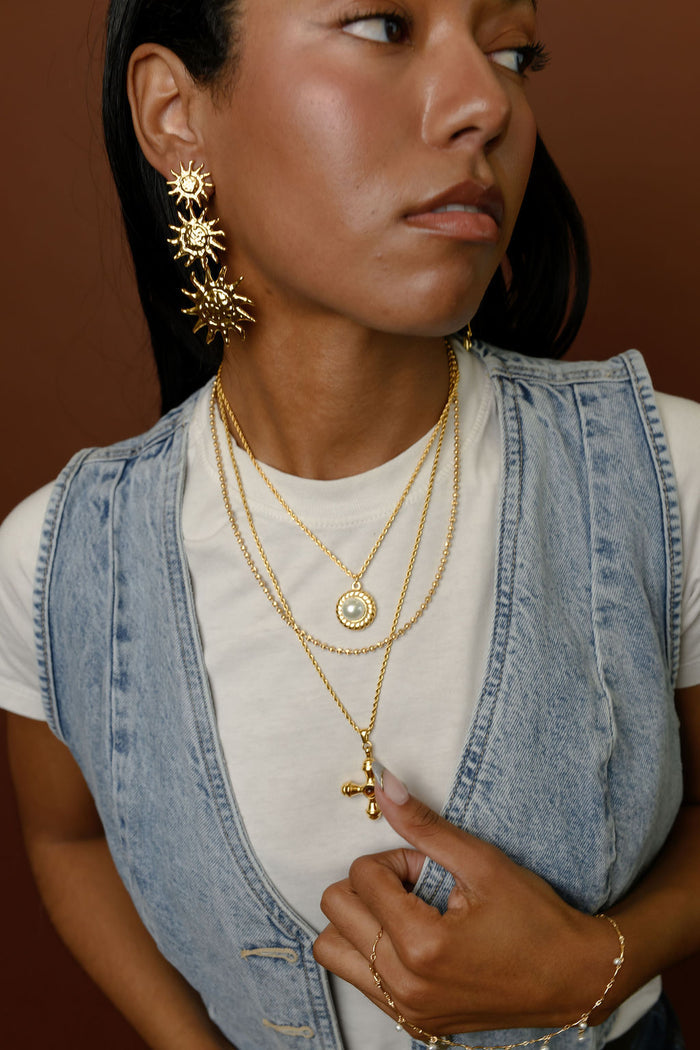 Woman wearing statement gold earrings and necklaces on a brown background