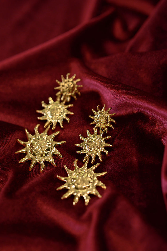Gold statement earrings on a red fabric background