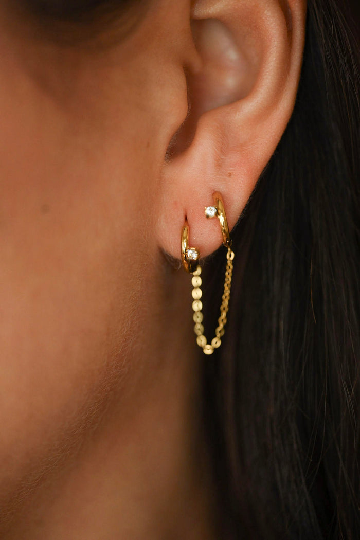 Gold hoop earrings worn by a person with dark hair.