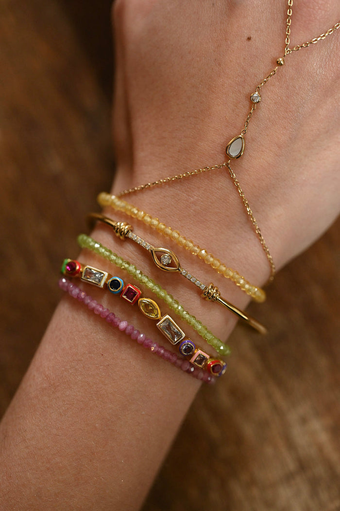 Close-up of a wrist wearing multiple gold and beaded bracelets on a wooden surface.