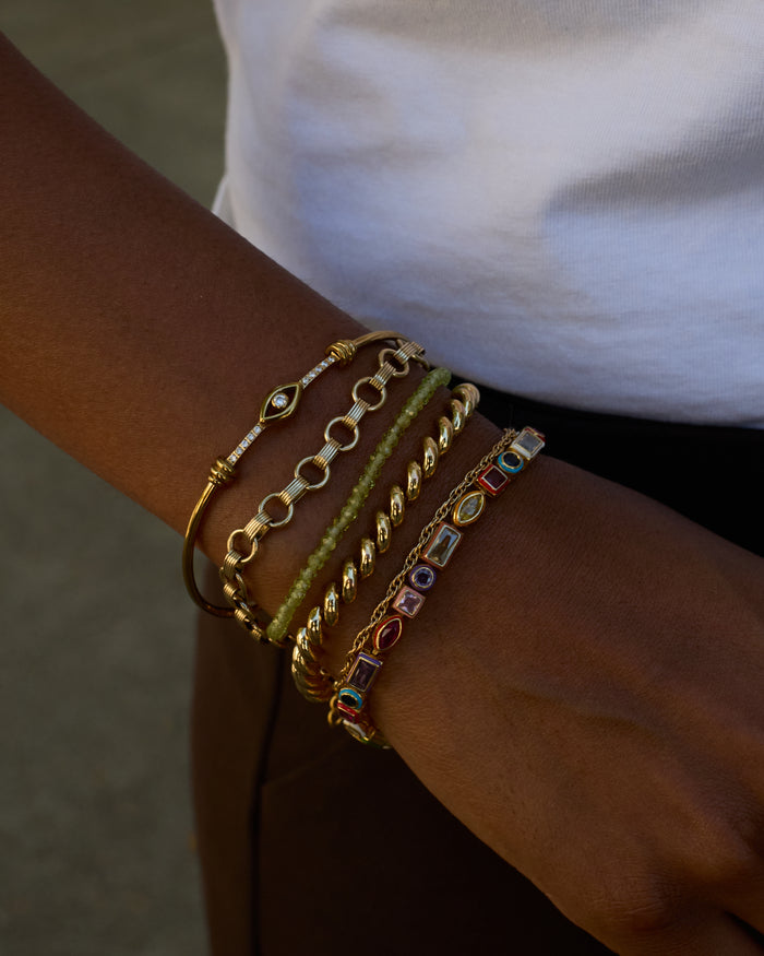 Close-up of a wrist wearing multiple gold and colorful bracelets on a blurred background