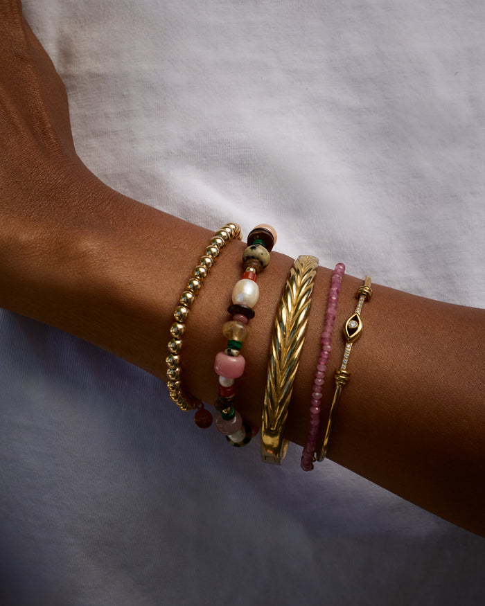 Close-up of a wrist wearing multiple gold and beaded bracelets on a neutral background