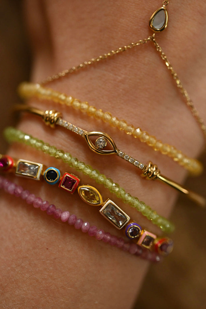 Close-up of a wrist wearing multiple gold and gemstone bracelets on a blurred background