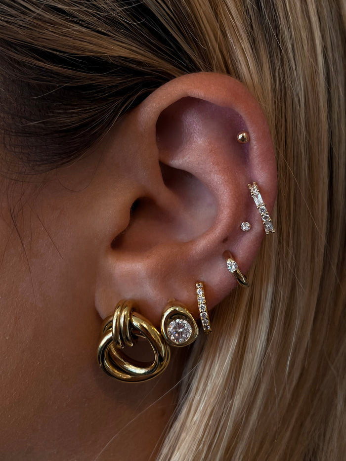 Close-up of an ear with multiple gold and crystal earrings