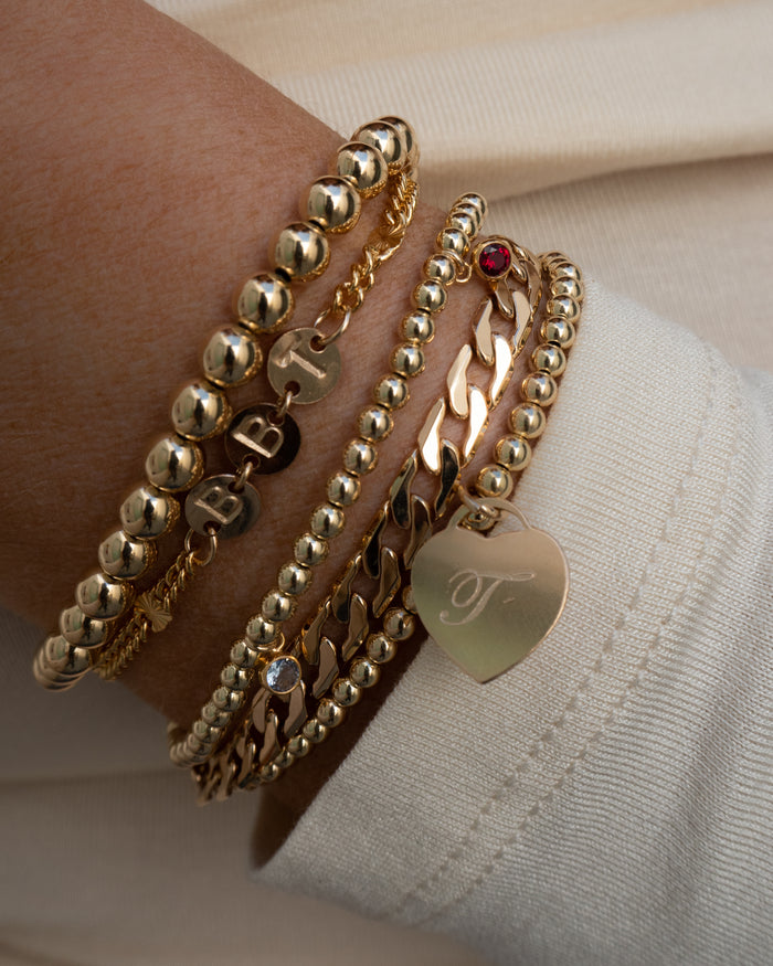 Close up of a wrist in a white sweater with assorted gold bracelets