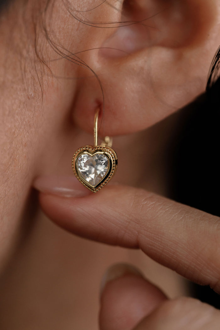 Close-up shot of heart-shaped gold earring on ear with a finger supporting it