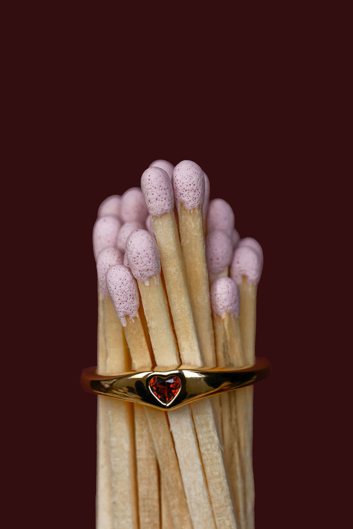 Matchstick with a gold ring featuring a red gemstone on a dark background