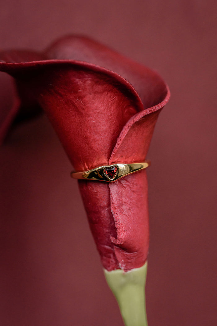 Gold ring with a heart design on a red flower against a red background