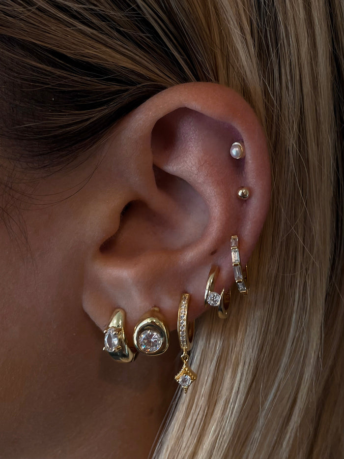 Close-up of an ear with multiple gold and crystal earrings
