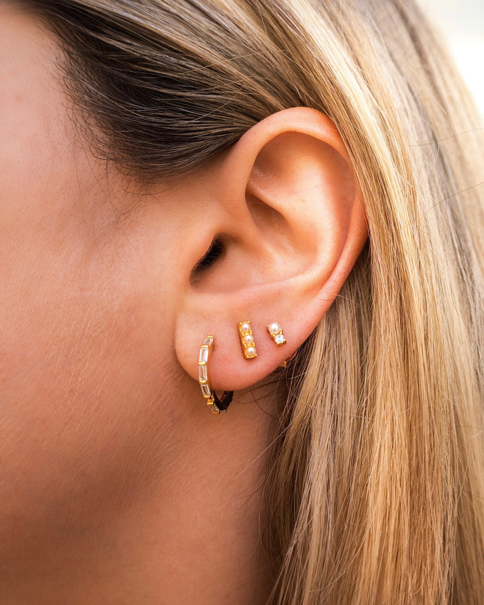 Close-up of an ear with multiple gold and crystal earrings