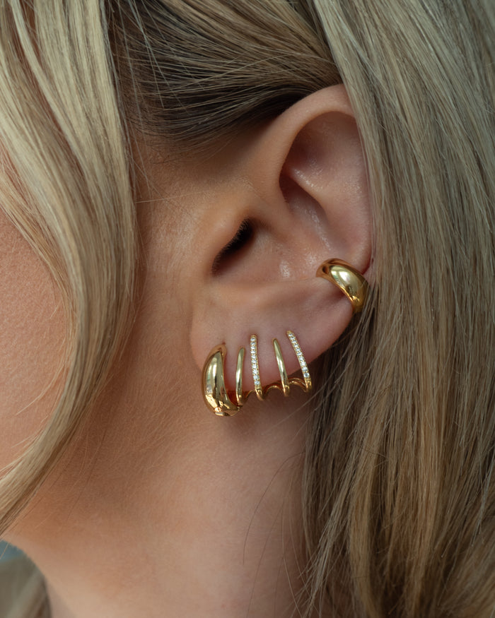 Close-up of an ear with multiple gold and crystal hoop earrings