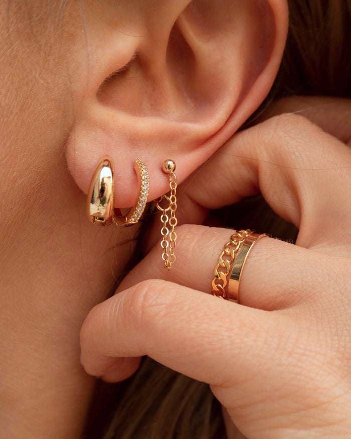 Close-up of an ear and a hand with multiple gold and crystal earrings and rings