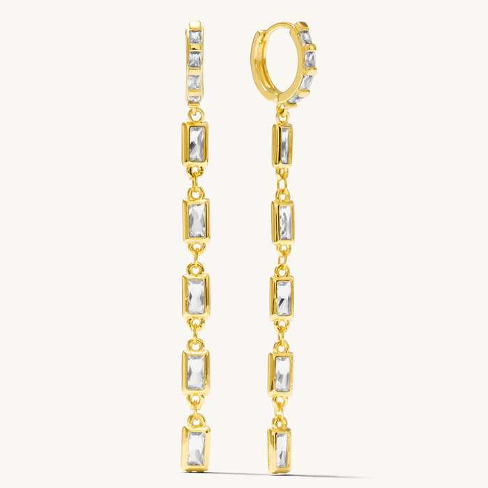 close up of gold stone dangle earrings on a white background