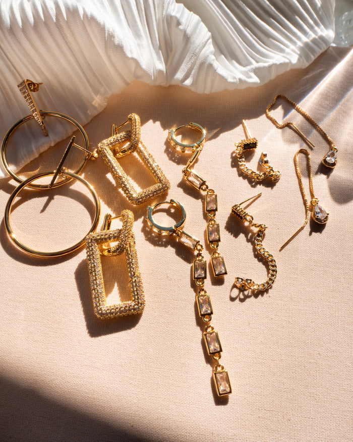 Five pairs of gold stone earrings on a neutral background with a white cloth