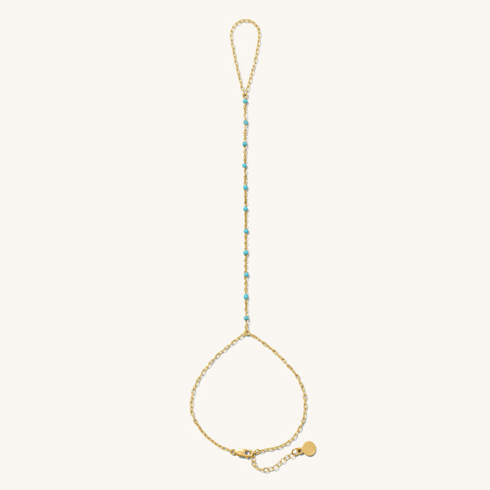 Close up of gold hand chain with teal bead accents on a white background